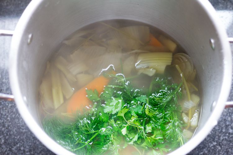 Stock pot with mirepoix vegetable stock and fresh herbs added after simmering