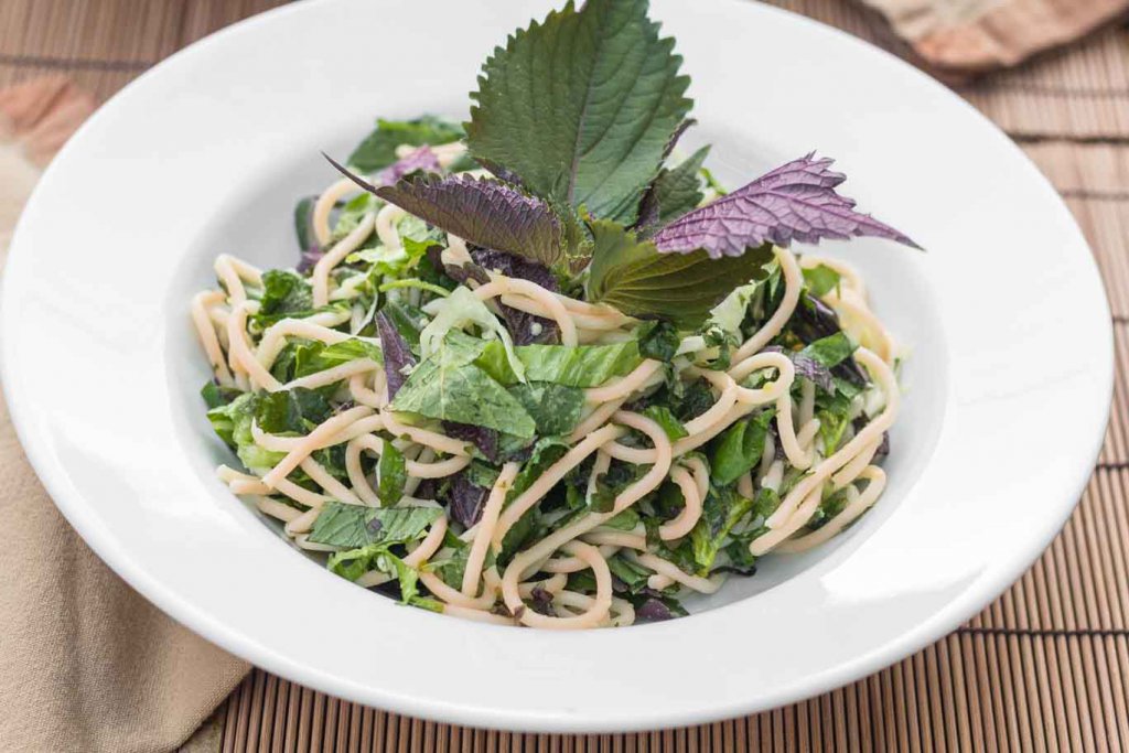 Large white rimmed bowl with Asian Herbs & Noodles, garnished with whole purple and green perilla leaves.