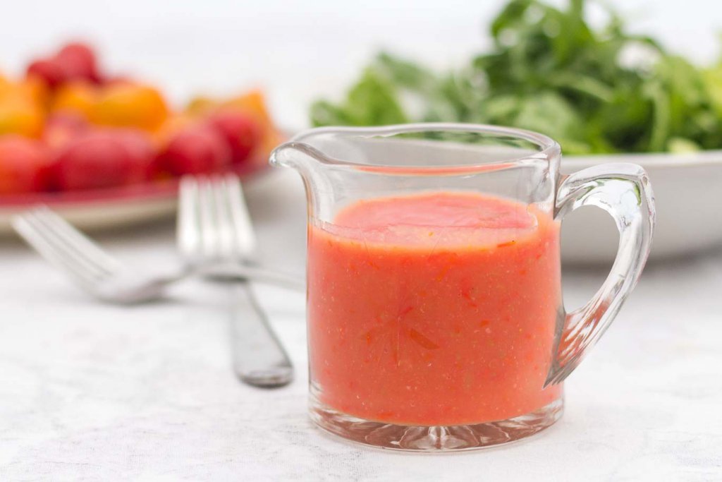 Glass cup with spout containing Bright Summer Oil-free Tomato Salad Dressing in an elegant glass pouring vessel.