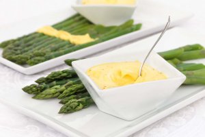Silky smooth oil-free vegan hollandaise in a square white bowl served with blanched asparagus on white rectangular plates.