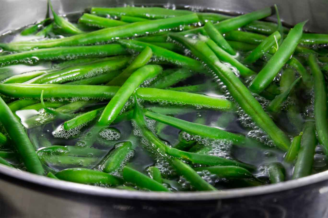 Pot of simmering water with green beans showing how blanching green vegetables keeps the color vibrant green.