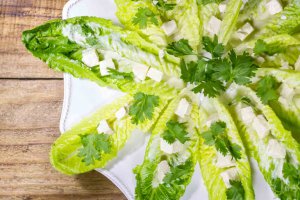 A white platter with whole romaine leaves with a layer of vegan feta tangy bites, cilantro, dressed with oil-free vegan citrus garlic dressing