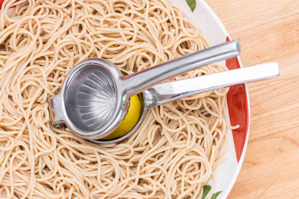 Squeezing lemon juice with a Stainless Steel Lemon Squeezer over a bowl of pasta.
