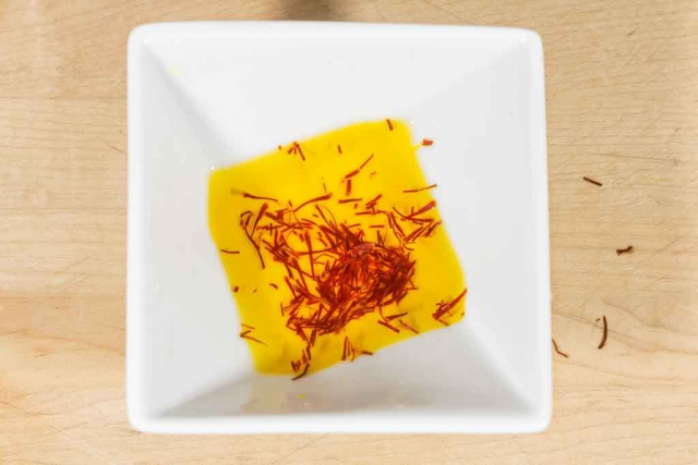 White bowl with saffron threads and warm water turning golden yellow