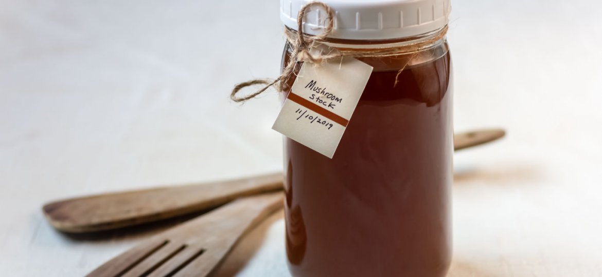 Mason jar filled with Caramelized Mushroom Stock, and a date and title tag on the jar next to 2 wooden spatulas o