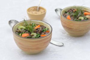 Two ceramic bowls of Mirepoix lentil soup garnished with fennel fronds and a small bowl of salt-free spiced cashew blend behind Mirepoix