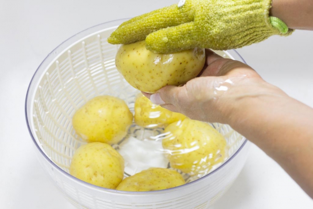 Scrubbing whole Yukon Gold potatoes in a salad spinner bowl using scrub gloves