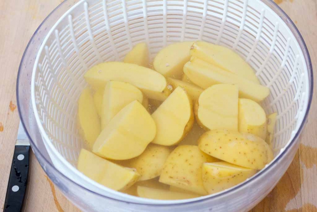 Salad spinner bowl filled with clean water to rinse the cut potatoes
