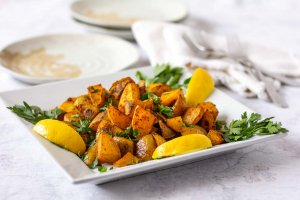 Square white plate with Turmeric spiced Oil-free Roasted Potatoes garnished with 3 lemon slices and parsley