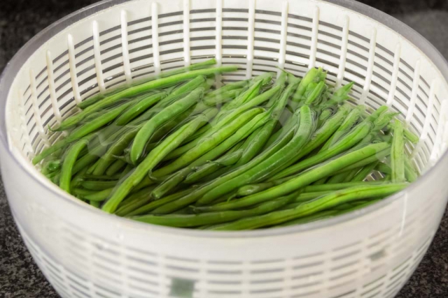 Green beans in a salad spinner filled with water to wash