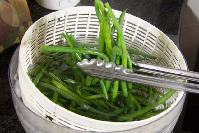 Green beans being put into ice bath bowl with tongs