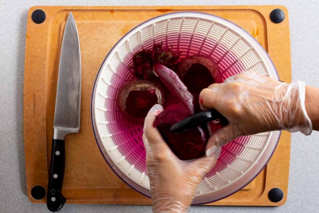 Peeling the skin off a red beet over the salad spinner bowl of water