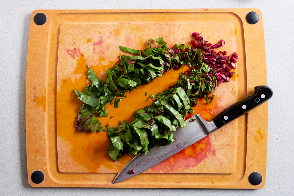 Beet greens cut lengthwise on a cutting board with a chef knife