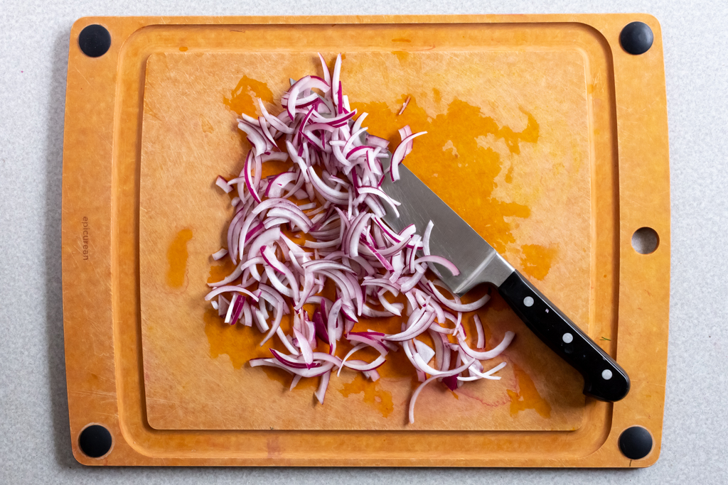 Thinly sliced onions on a cutting board with a chef knife
