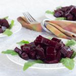 Braised beets on a white Wedgewood plate garnished with arugula with 2 additional plates behind