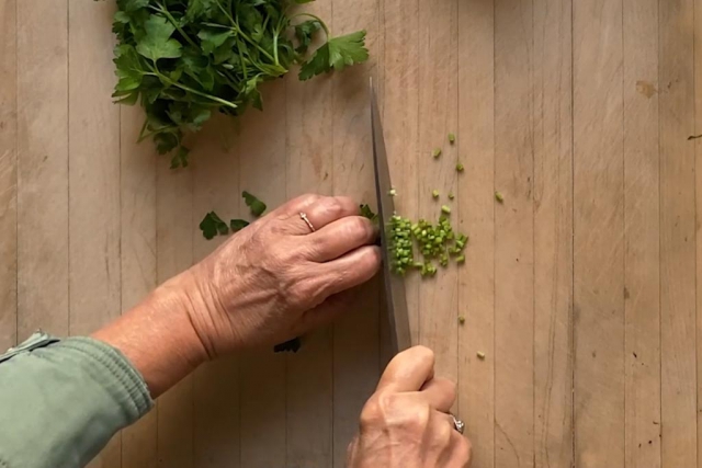 Cutting parsley stems with a chef knife into 1/8 pieces on a large wood cutting board