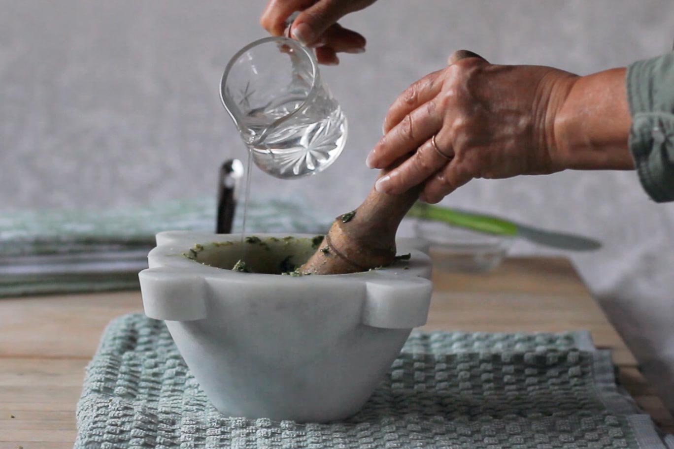 Pouring water from a small glass pitcher into the marble mortar on a board