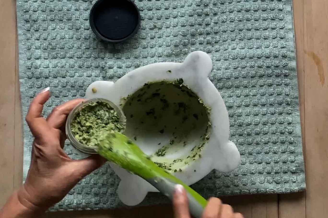 Using a silicone spatula to remove pesto from mortar and place into a small glass jar