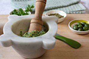 Parsley and Pumpkin seed pesto in the marble mortar with the wood pestle on a cutting board small bowls of Castelvetrano olives, pumpkin seeds and parsley leaves